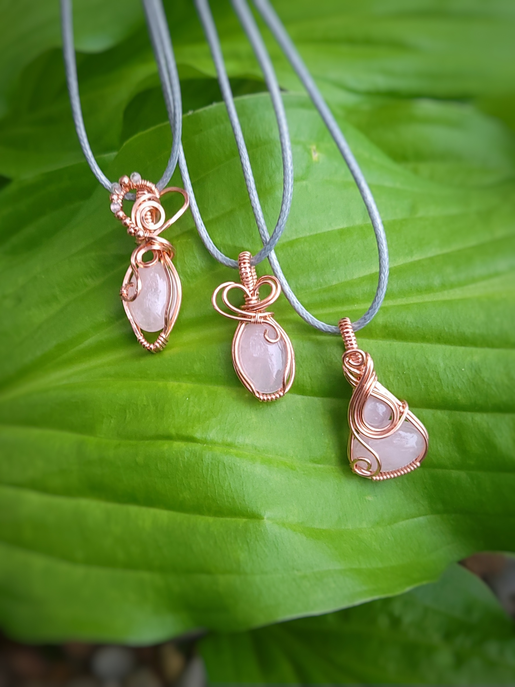 Handcrafted rose quartz pendants wrapped in bare copper and arranged on a leaf.