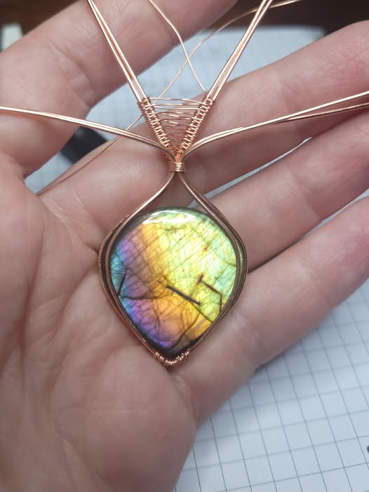 A rainbow labradorite in the process of being wrapped in bare copper wire with a woven bail.